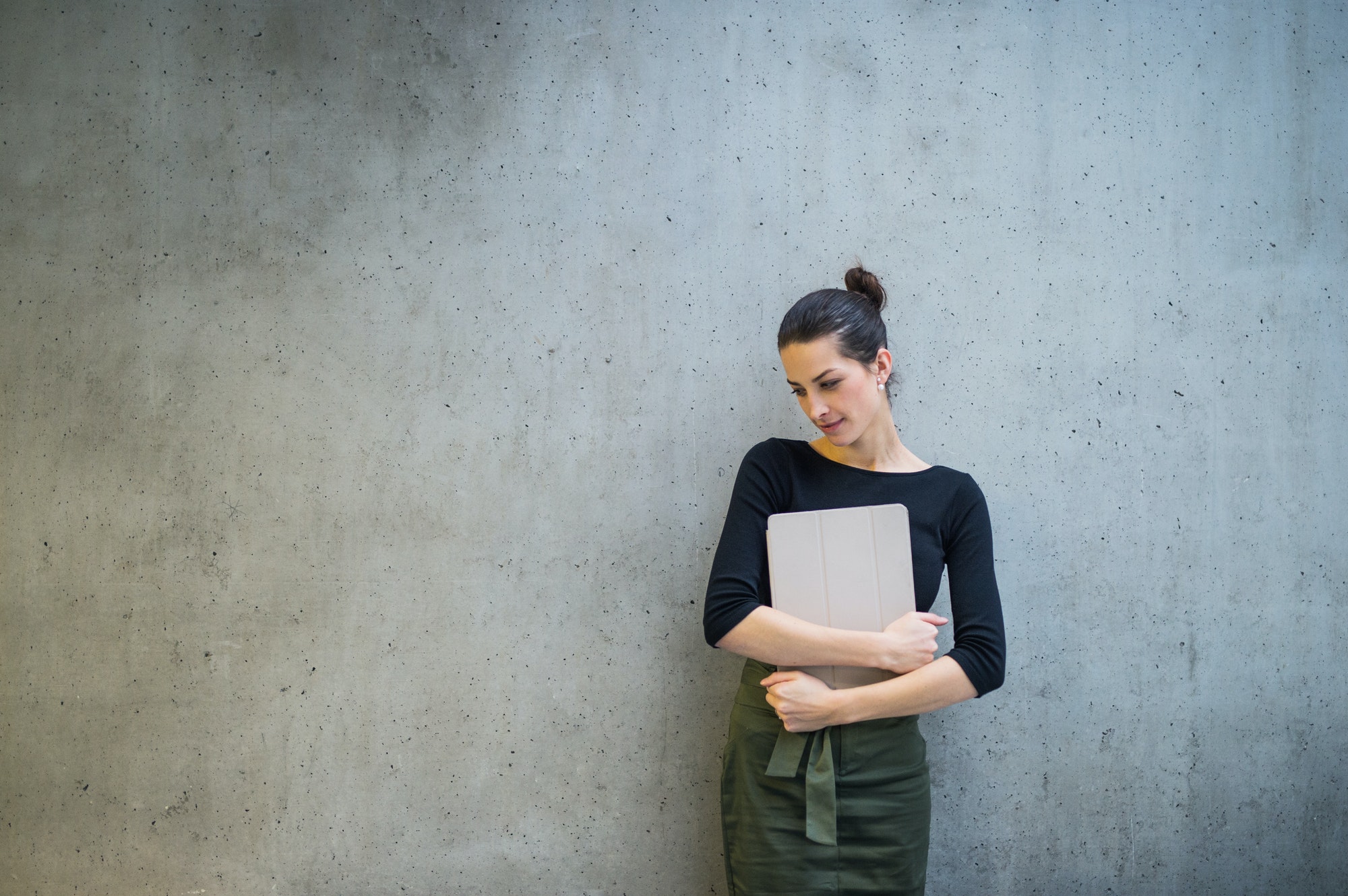 Young business woman with tablet standing against concrete wall in office.